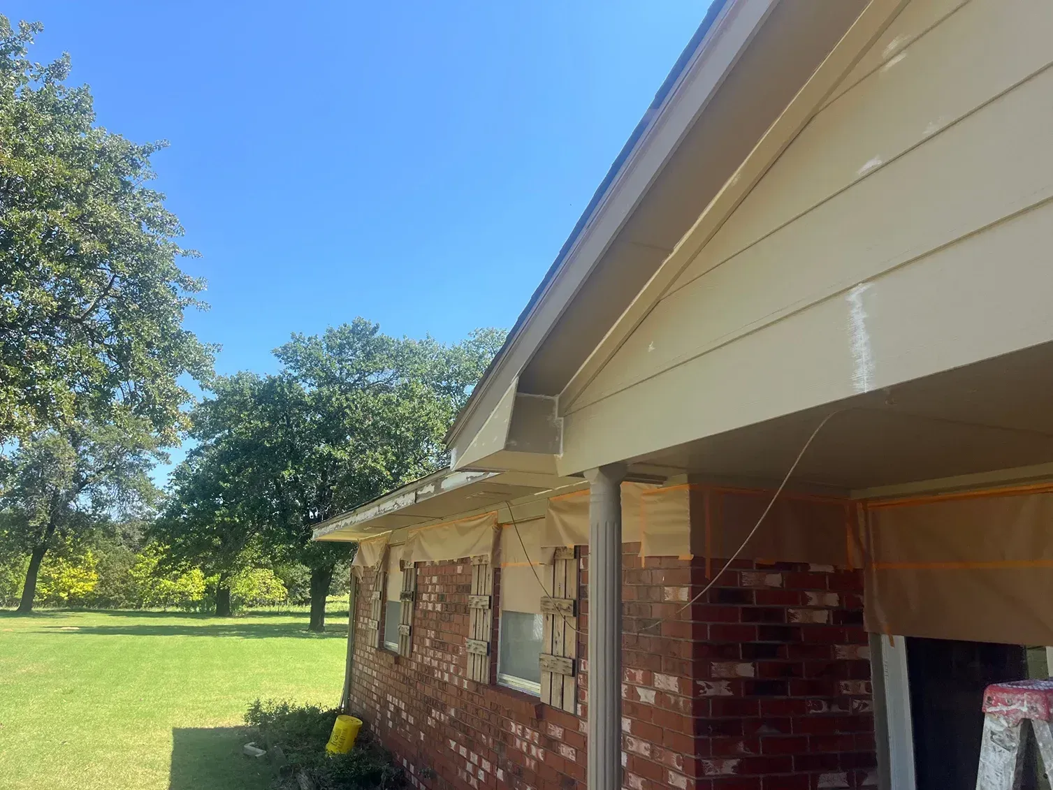 Exterior of a brick house with tan siding and a clear blue sky. Green grass and trees in the background.