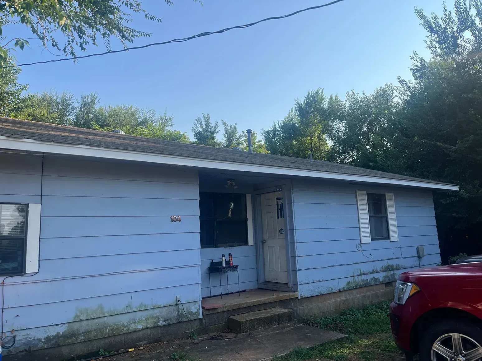 Blue house with white trim, gray roof, and trees in the background under a blue sky.