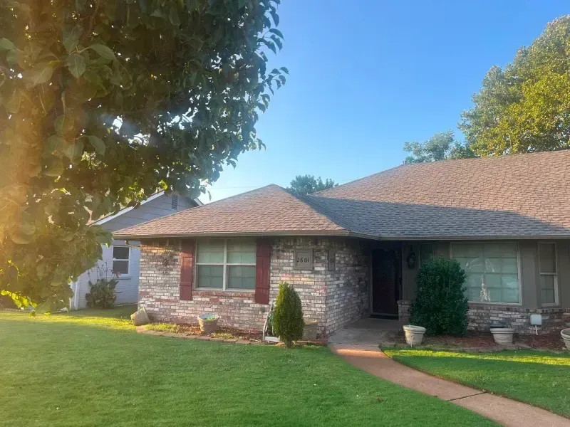 House with brick exterior, brown roof, and green lawn. Pathway leads to a dark door.