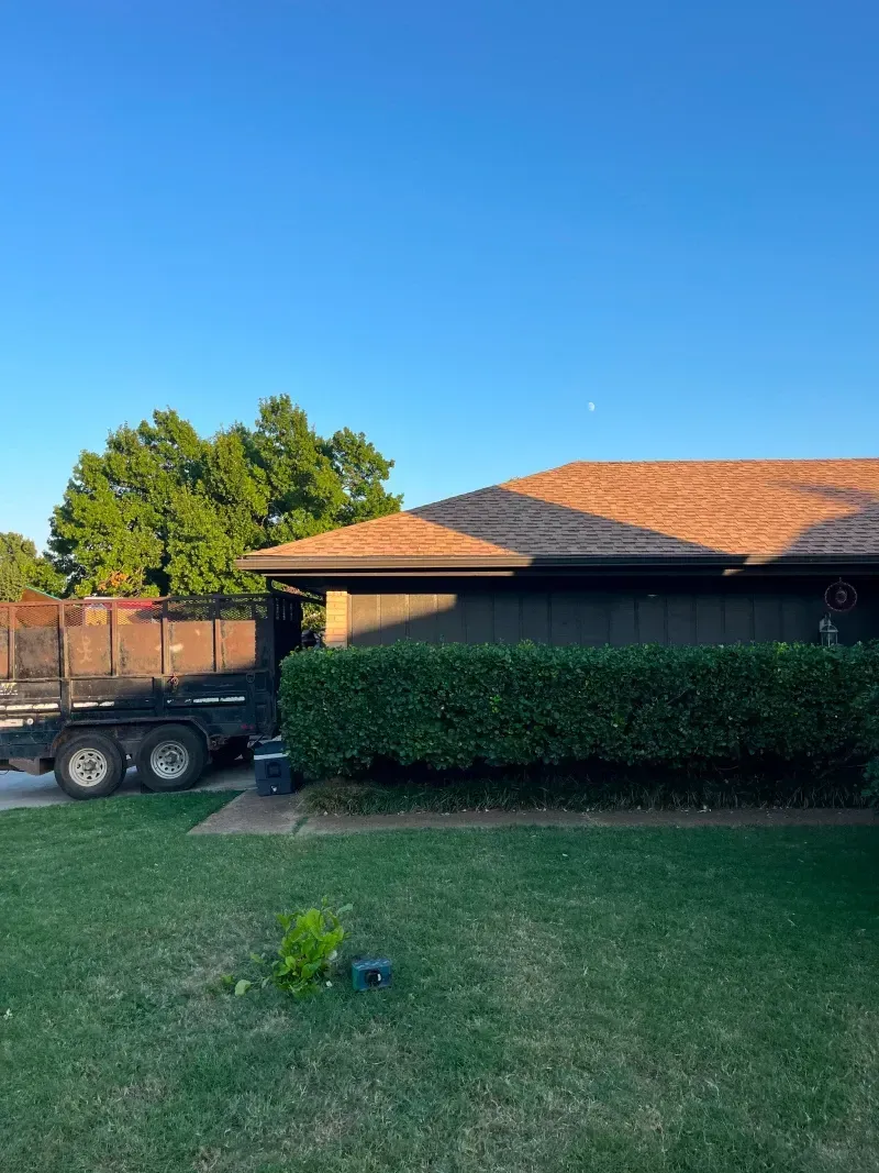 A trailer next to a house with a neatly trimmed hedge. Green lawn and a blue sky.