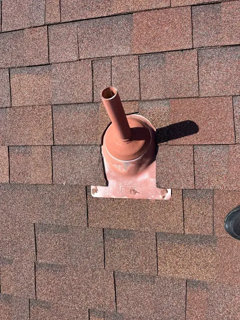 Orange vent pipe on a brown shingle roof, casting a shadow.