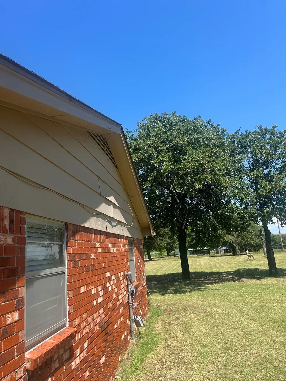 Brick building exterior with tan siding and green trees against a blue sky.
