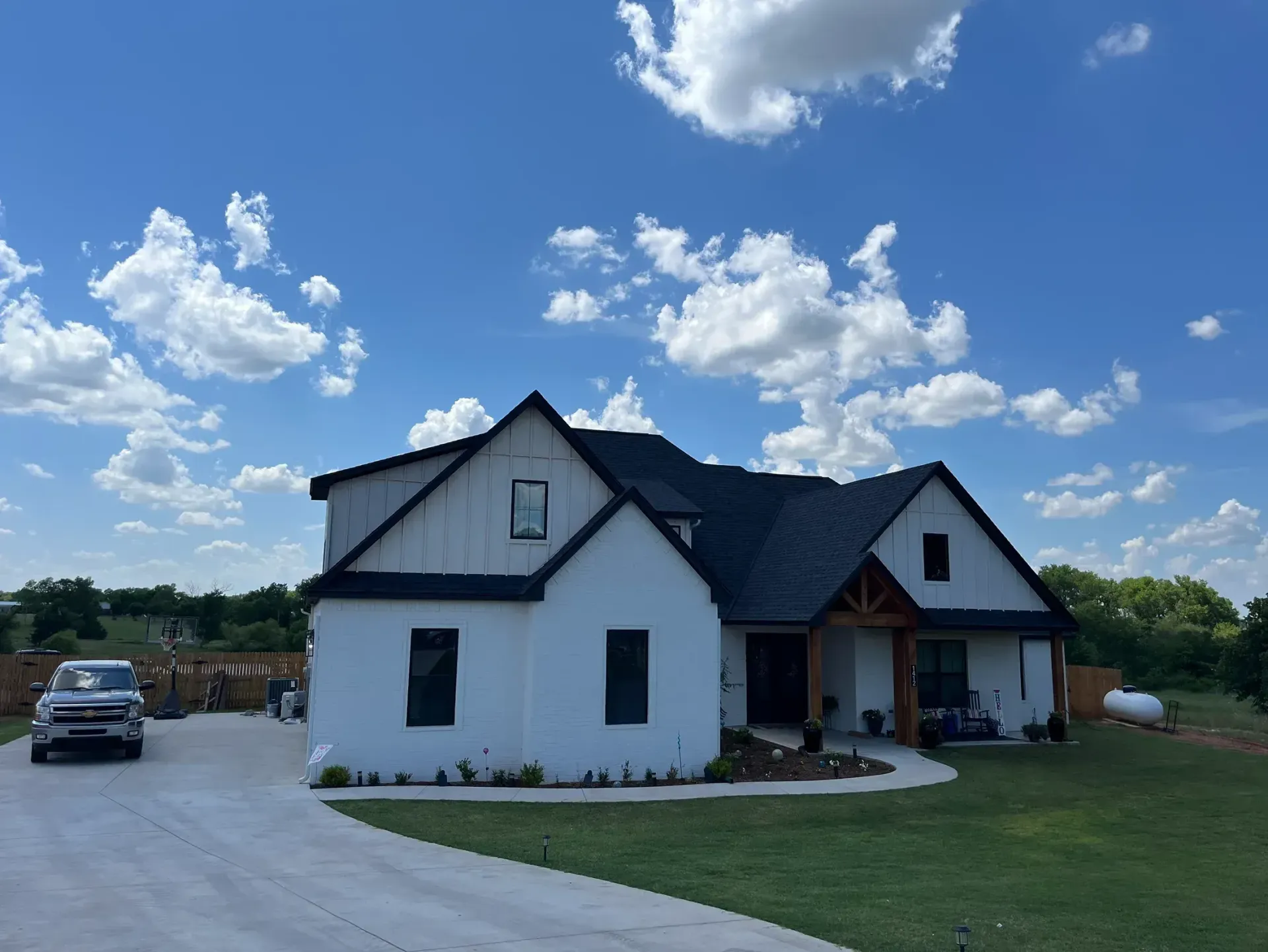 White farmhouse with black roof under a partly cloudy sky. Car in driveway.