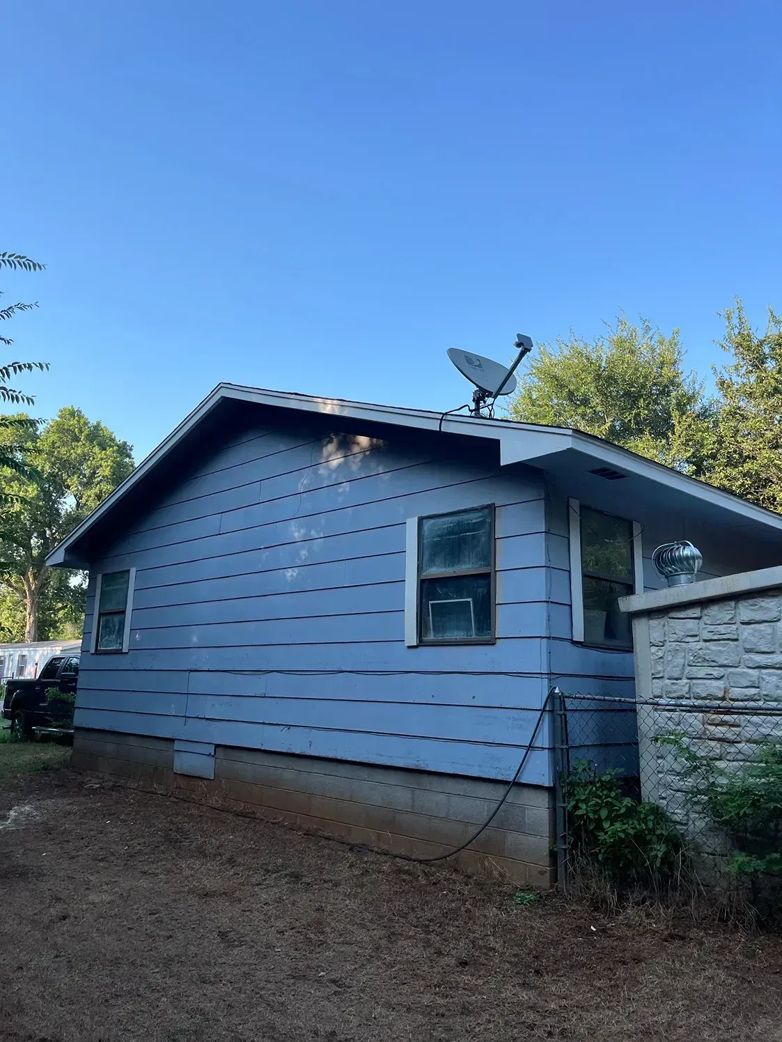 Blue house with satellite dish on the roof, two windows, and a stone wall in the yard.