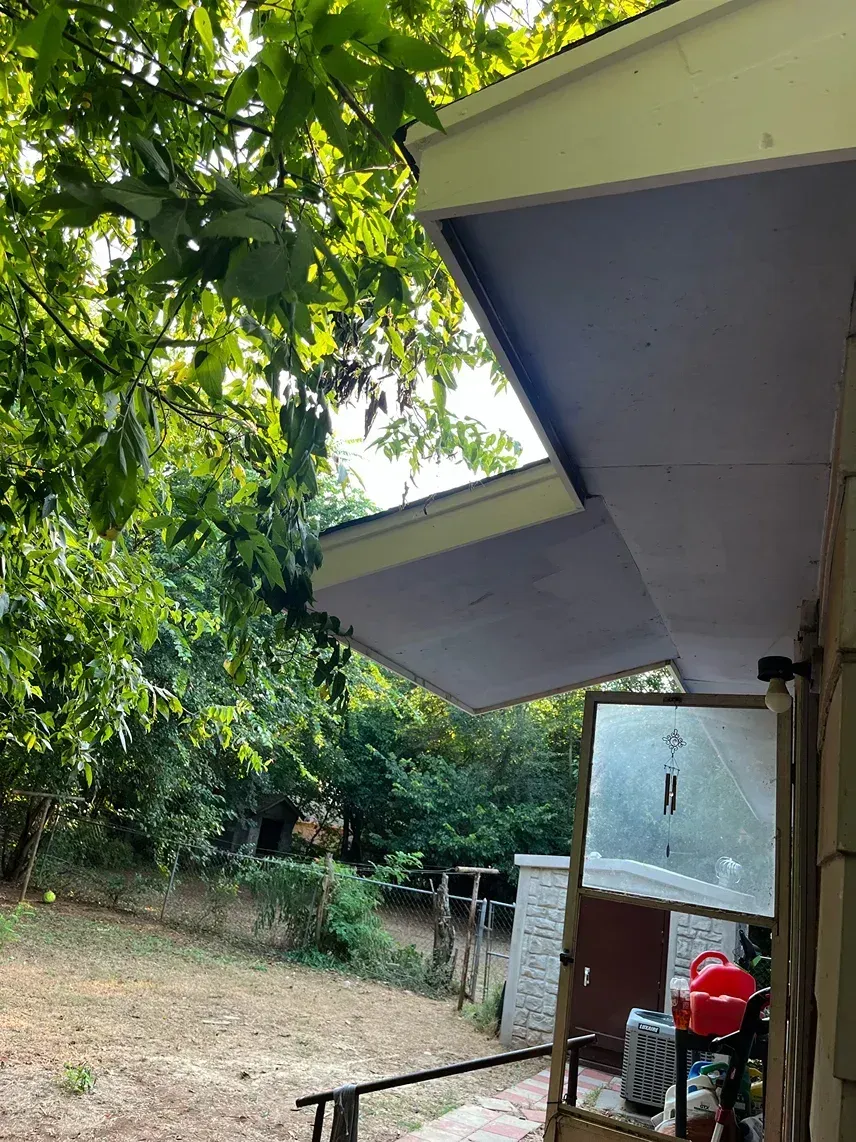 Overhanging porch roof with exposed underside, surrounded by greenery.