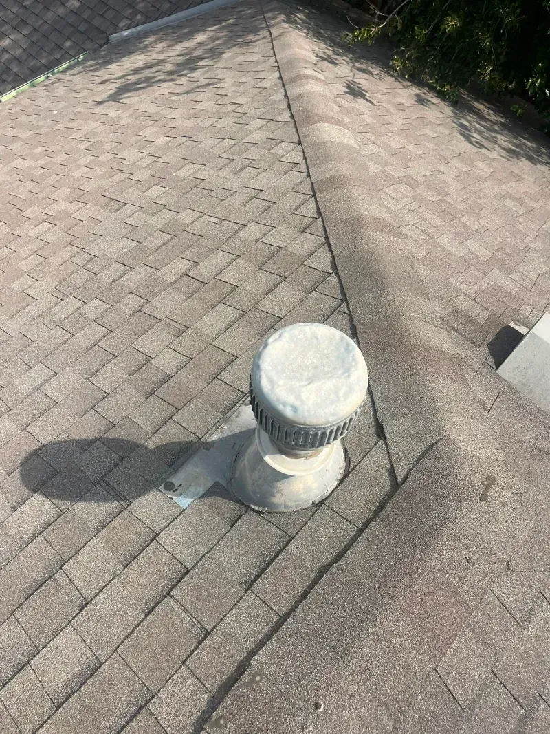 A roof with brown shingles and a gray rotary vent.