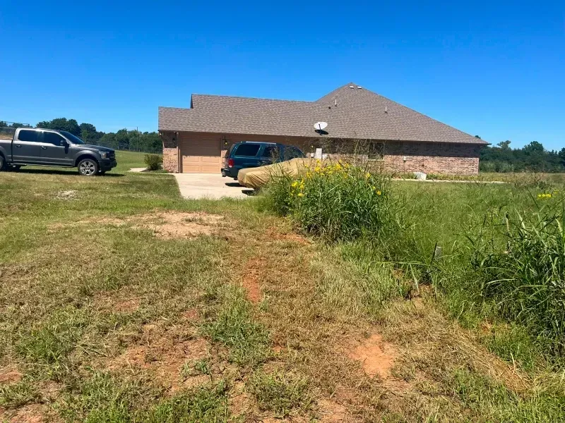 A house with a driveway and two vehicles in a grassy field on a sunny day.