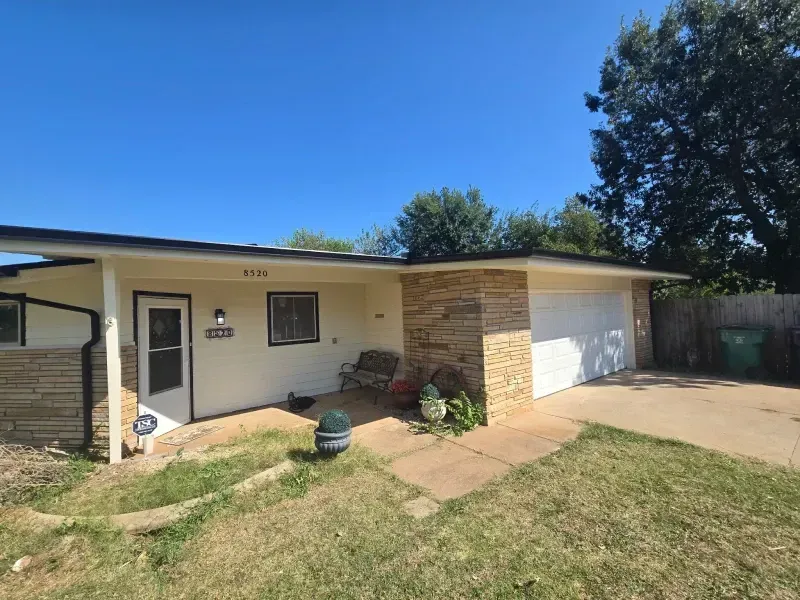 Beige house with a stone accent and a two-car garage under a bright blue sky.