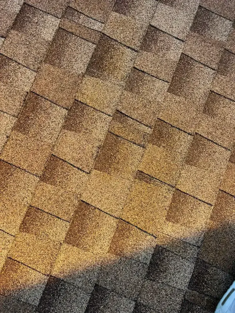 Close-up of brown asphalt roof shingles with light and shadow.