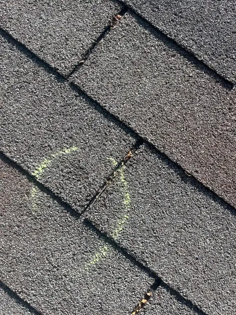 Close-up of gray asphalt roof shingles with a faint green circle drawn on them.