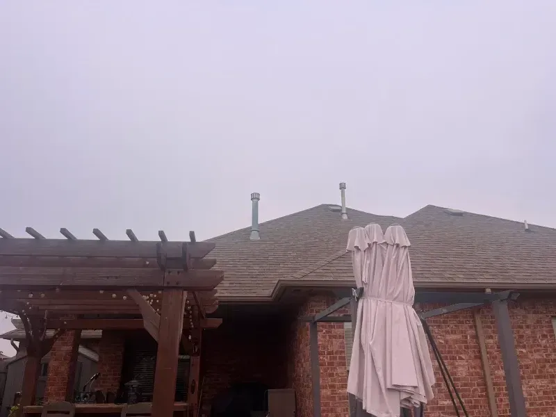 Brown house exterior with a pergola, chimney pipes, and a cloudy sky.