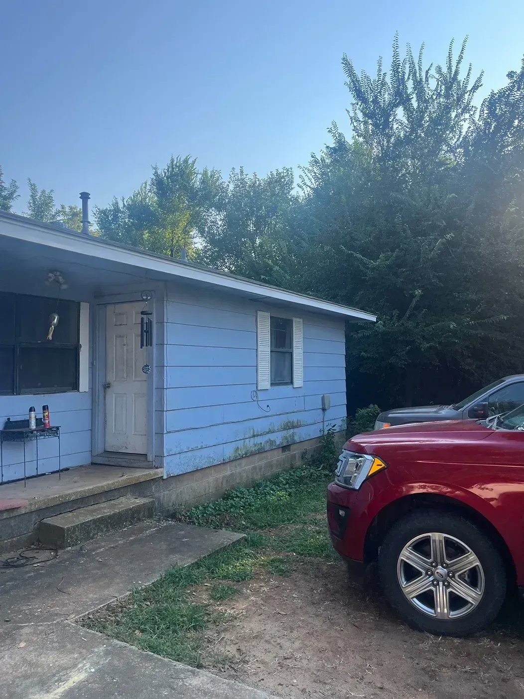 Blue house with a red car parked nearby on a sunny day.