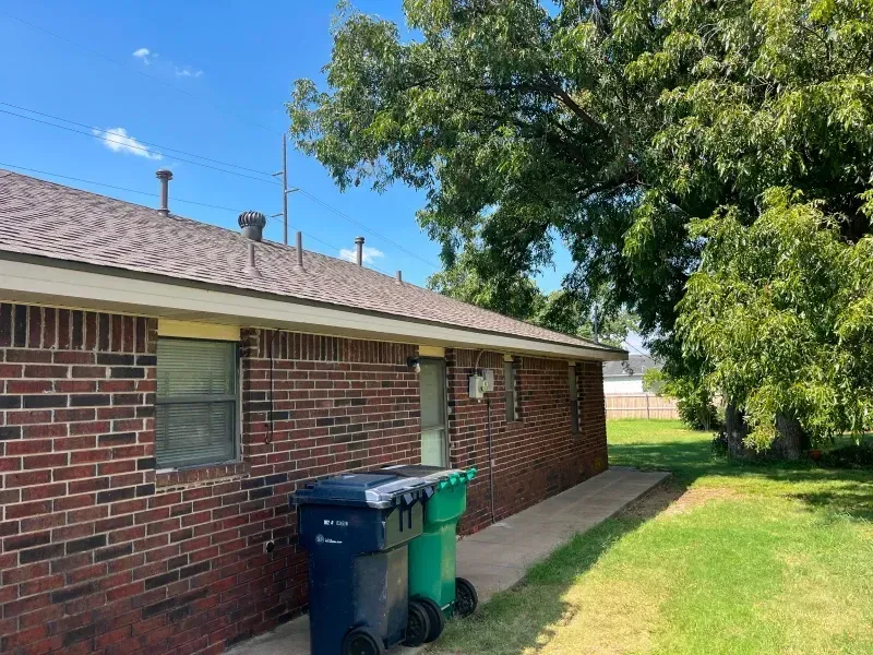 Brick house exterior with trash cans in the yard, tree, and blue sky.