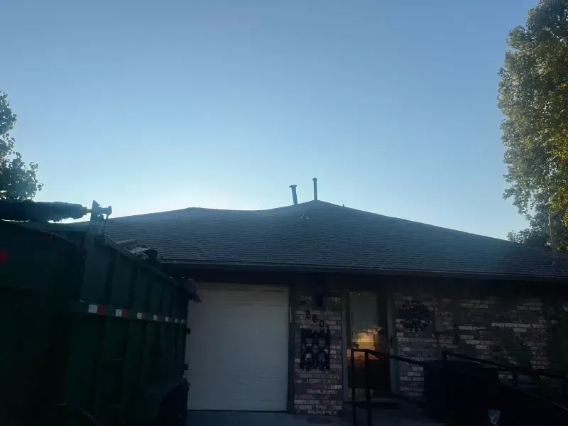 House exterior with dark roof and white garage door; a green dumpster on the left.
