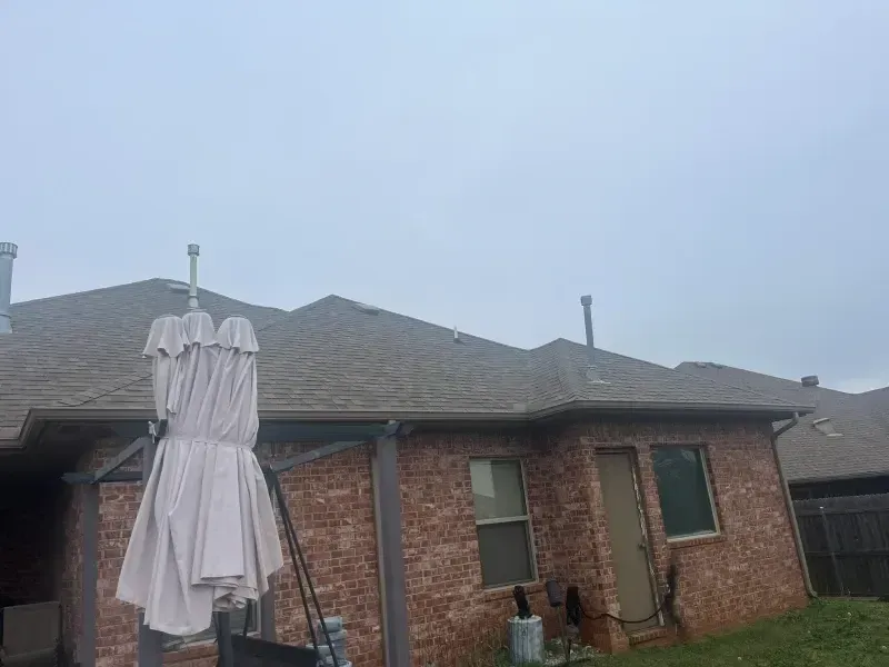 Red brick house with a brown roof and a closed white umbrella on a cloudy day.