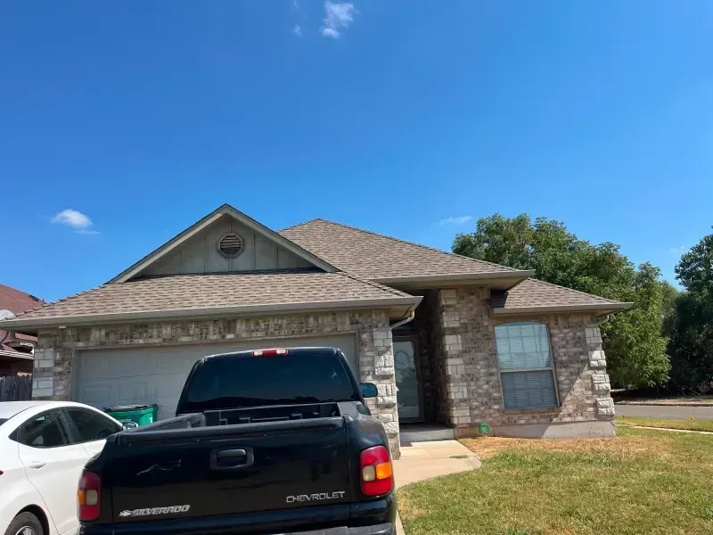 House with stone facade, brown roof, and black pickup truck parked in front on a sunny day.