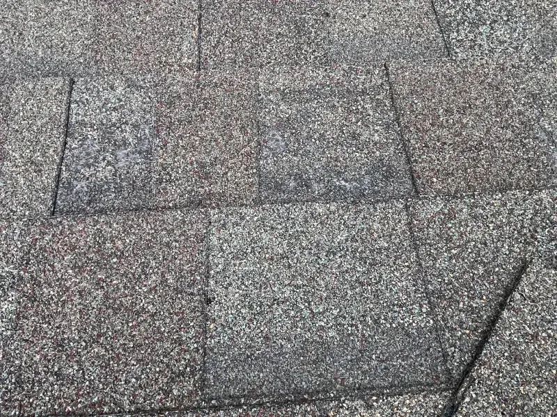 Close-up of asphalt roof shingles. Gray and brown granules cover the rectangular shapes.