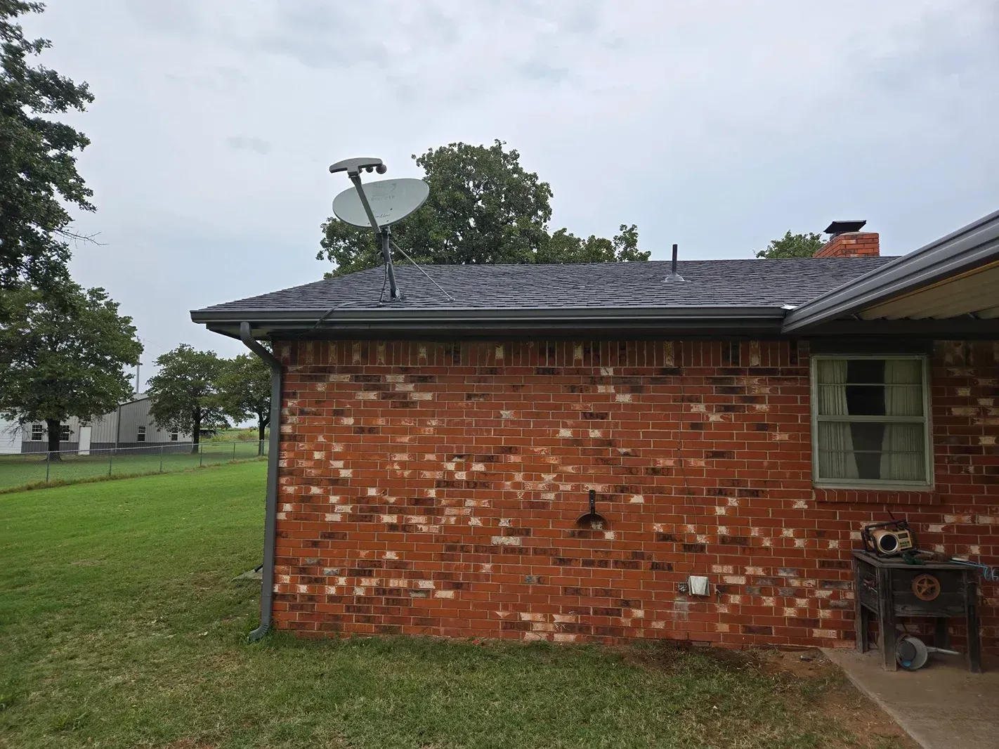 Brick house with satellite dish on the roof, overcast sky, green lawn.