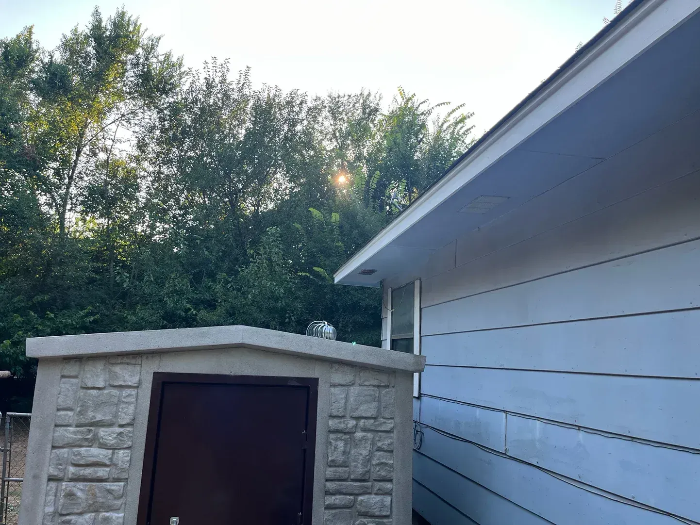 A light-colored building with a shed and trees in the background under a bright sky.