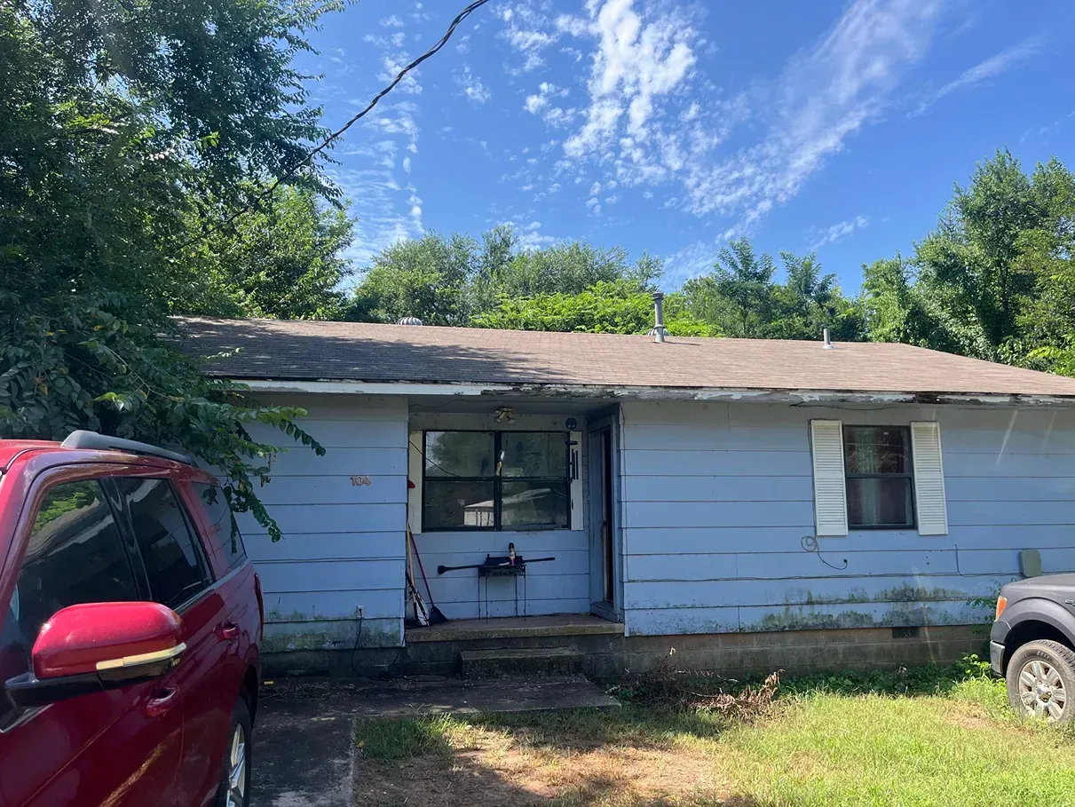 Blue house with weathered paint; a red car and black truck are parked outside.