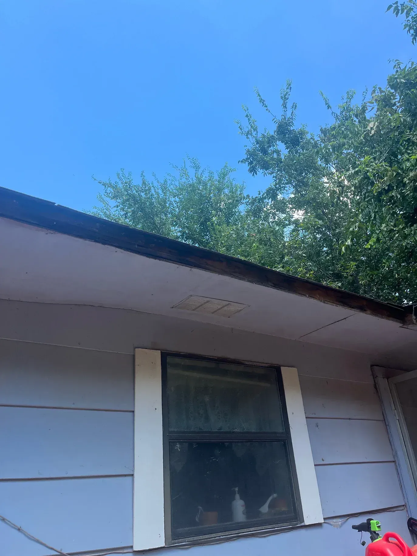 Exterior view of a house, with a window and overhanging roof. Blue sky and trees in the background.