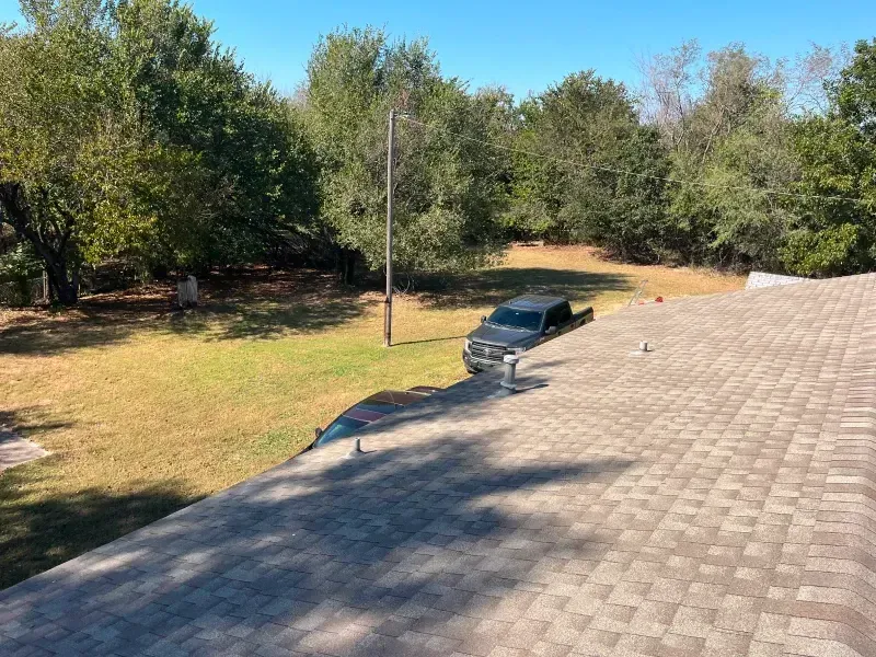 View from a roof, showing a gray truck on grass near a wooded area. Blue sky overhead.