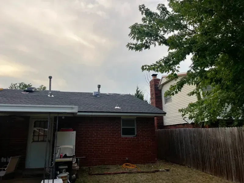 Red brick house with a dark roof and a neighboring white house; a wooden fence in the background.