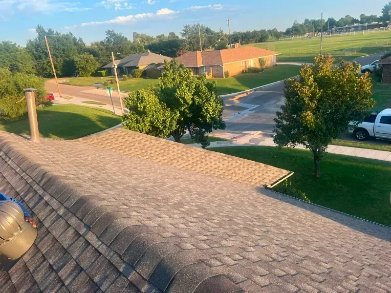 Rooftop view of a residential neighborhood with houses, trees, and streets under a blue sky.