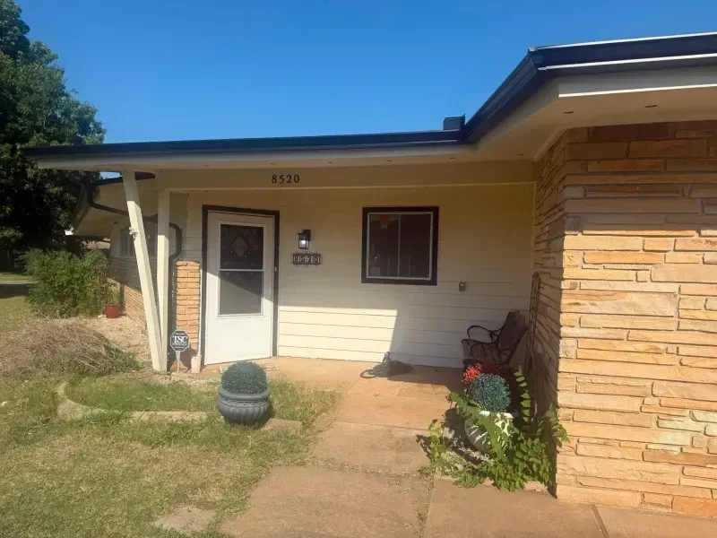A light yellow ranch-style house with a stone accent wall, a doorway, and a small window.