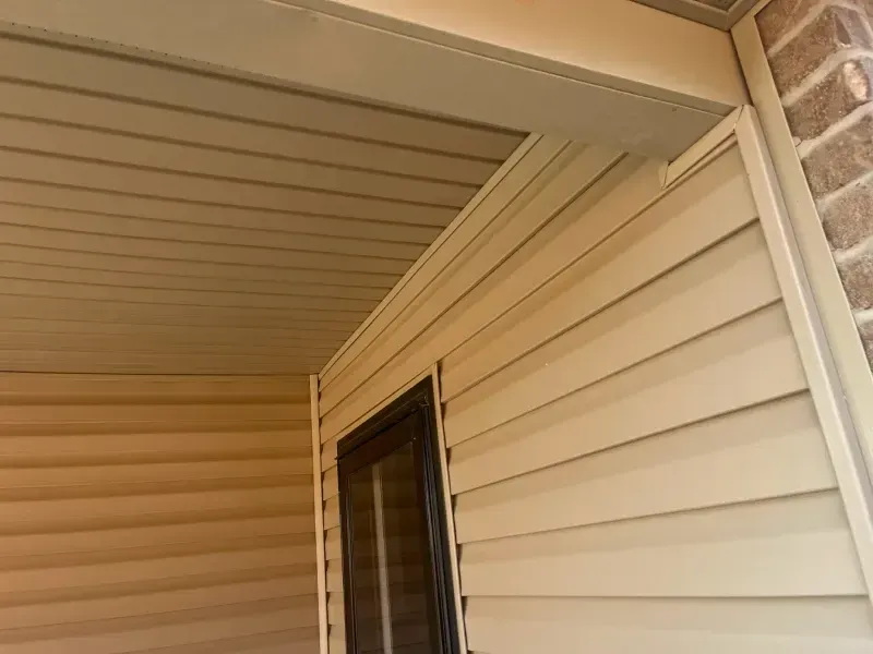 Beige siding and soffit on a building exterior, with a door and brick wall visible.