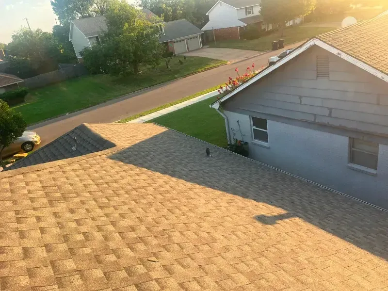 View from a roof of a house with brown shingles overlooking a street and other houses with green lawns.