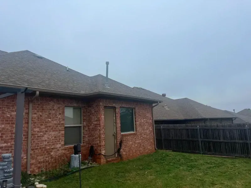 Brick house exterior with a green lawn, wooden fence, and gray sky.