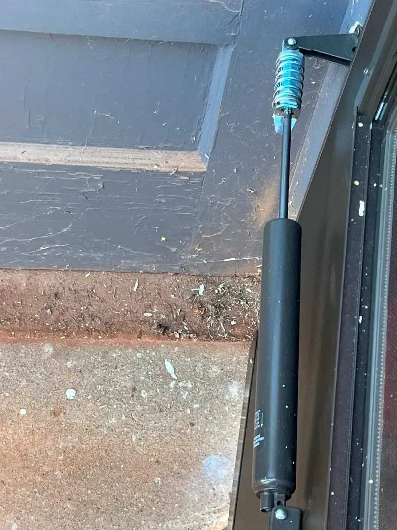 Black door with a spring-loaded door closer attached to the top edge; visible rust and peeling paint.