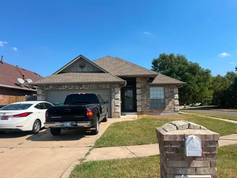 A brick-faced house with a black truck parked in the driveway on a sunny day.