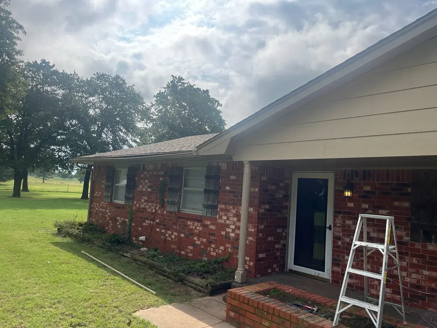 Red brick house with white trim, overcast sky, ladder leaning against the door.