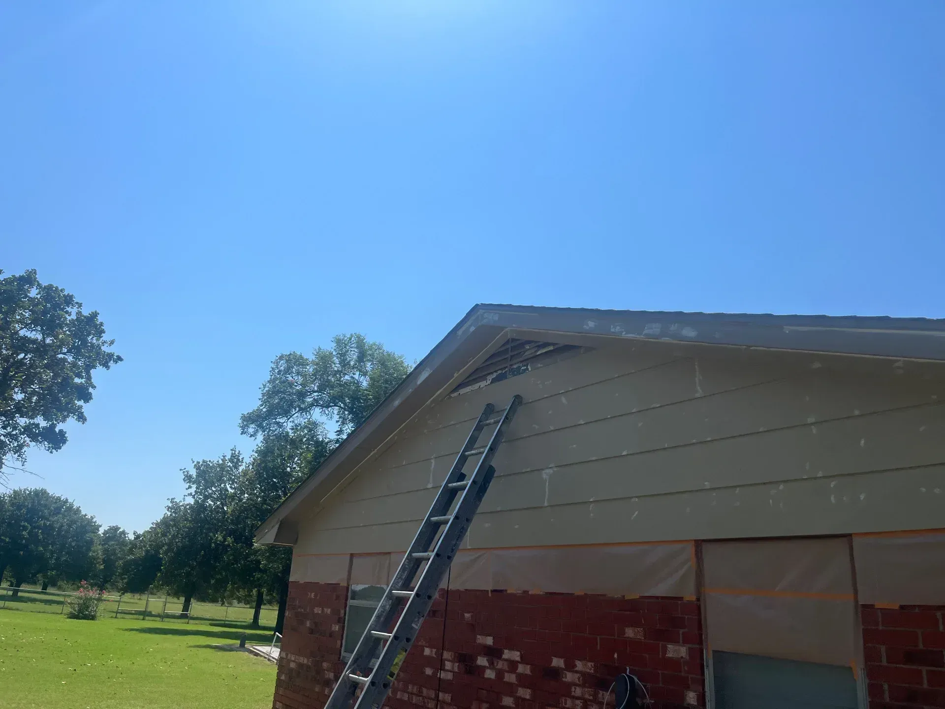 House exterior with ladder, tan siding, brick facade, blue sky.