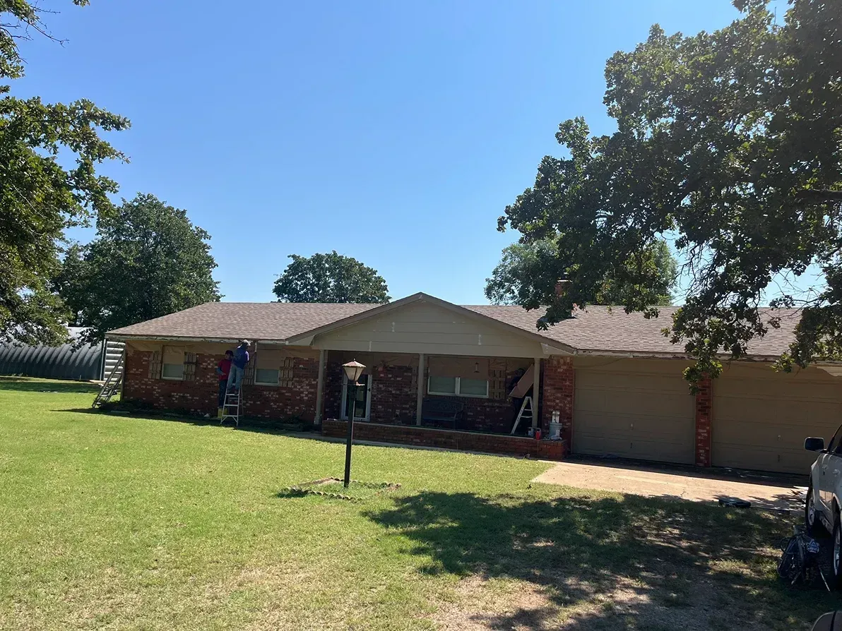 A one-story brick house with workers on ladders under a clear blue sky.
