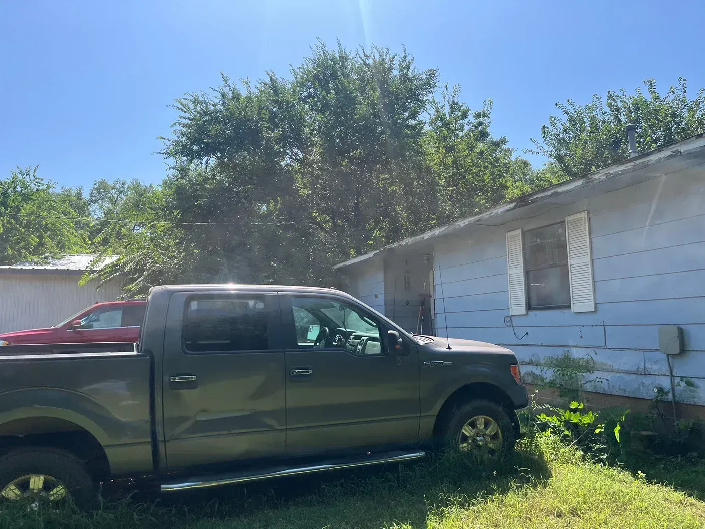 Green pickup truck parked near a light blue house on a sunny day.