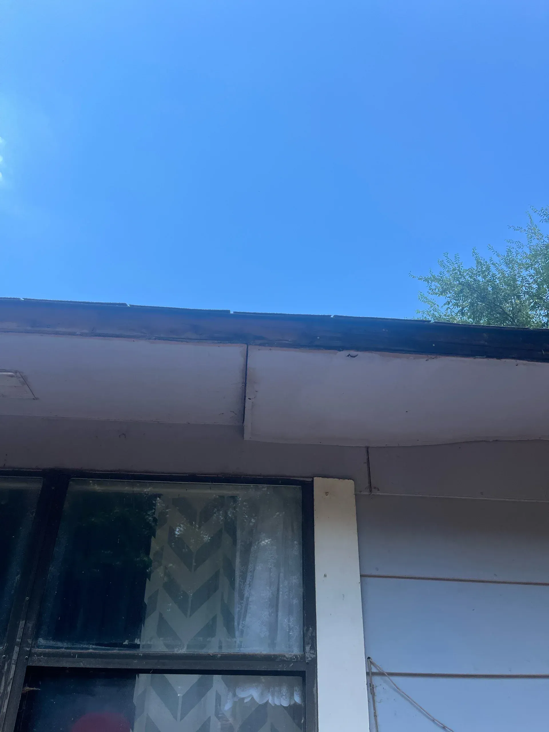 Eaves of a house against a blue sky. A window is visible below the eaves.