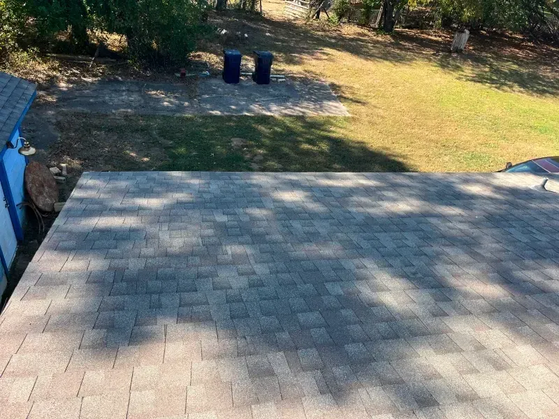Roof with mottled gray shingles, overlooking a yard with two blue trash cans.