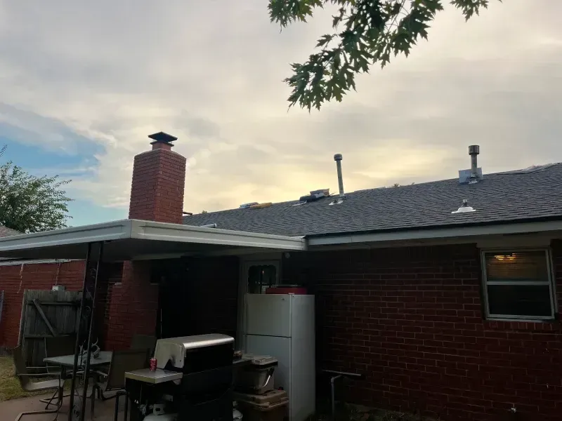 Brick house exterior with a chimney, a covered patio, and a cloudy sky.