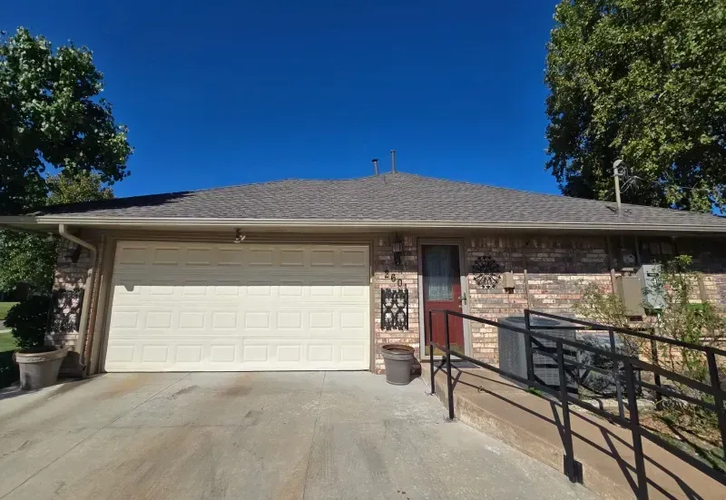 Exterior view of a brick building with a garage, entry door, and ramp. Blue sky background.