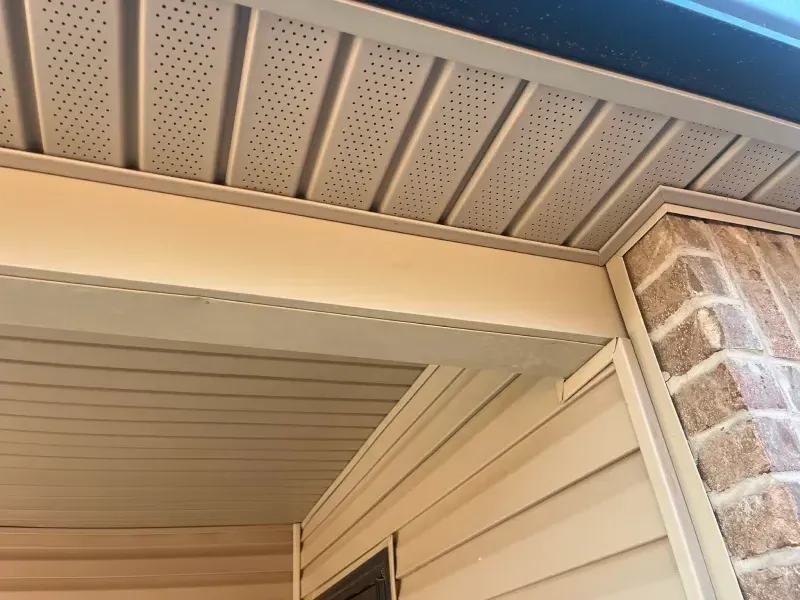 Beige siding and soffit on a building with brick corner and tan trim.