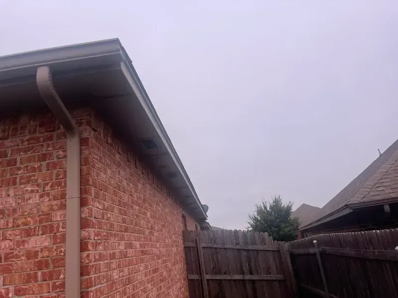 Red brick building with brown trim, gutters, and fence, under a cloudy sky.
