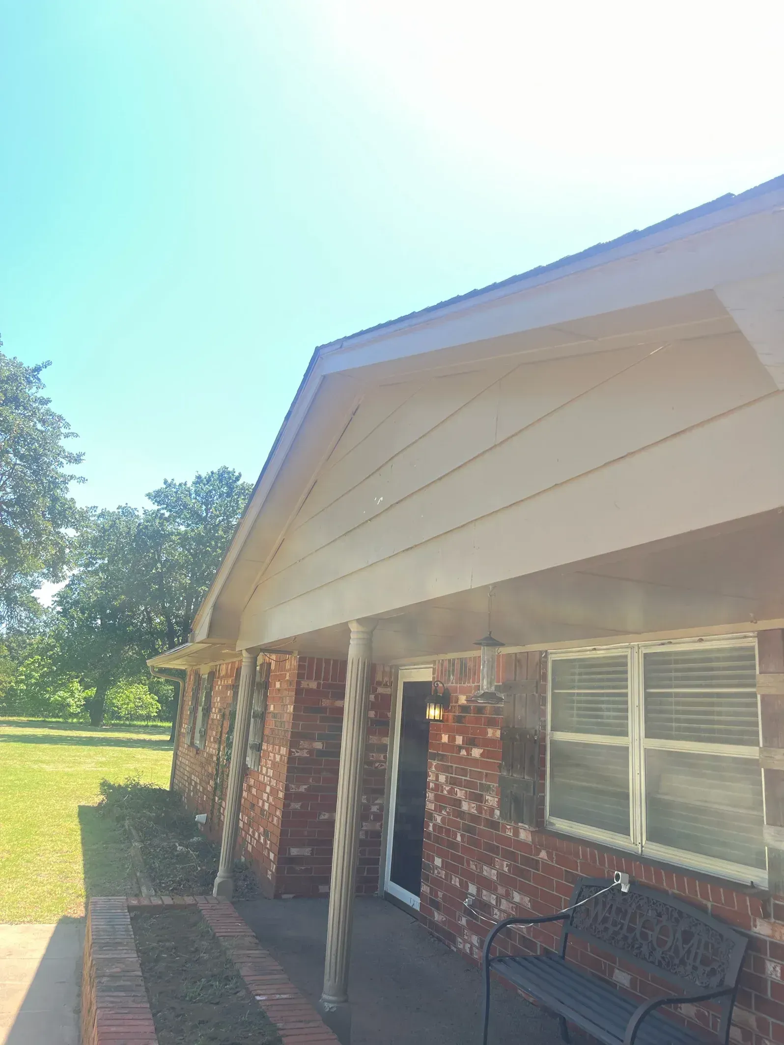 Brick house with white trim, a porch, and a clear blue sky.