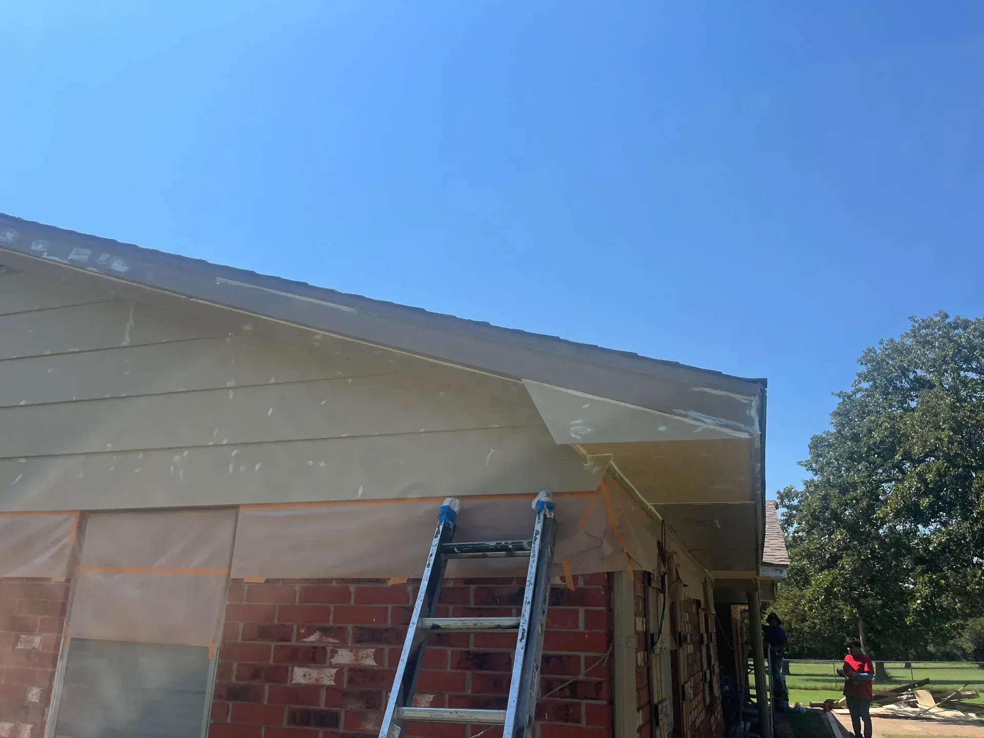 House exterior with ladder against the side, clear blue sky. Brick and light colored siding.
