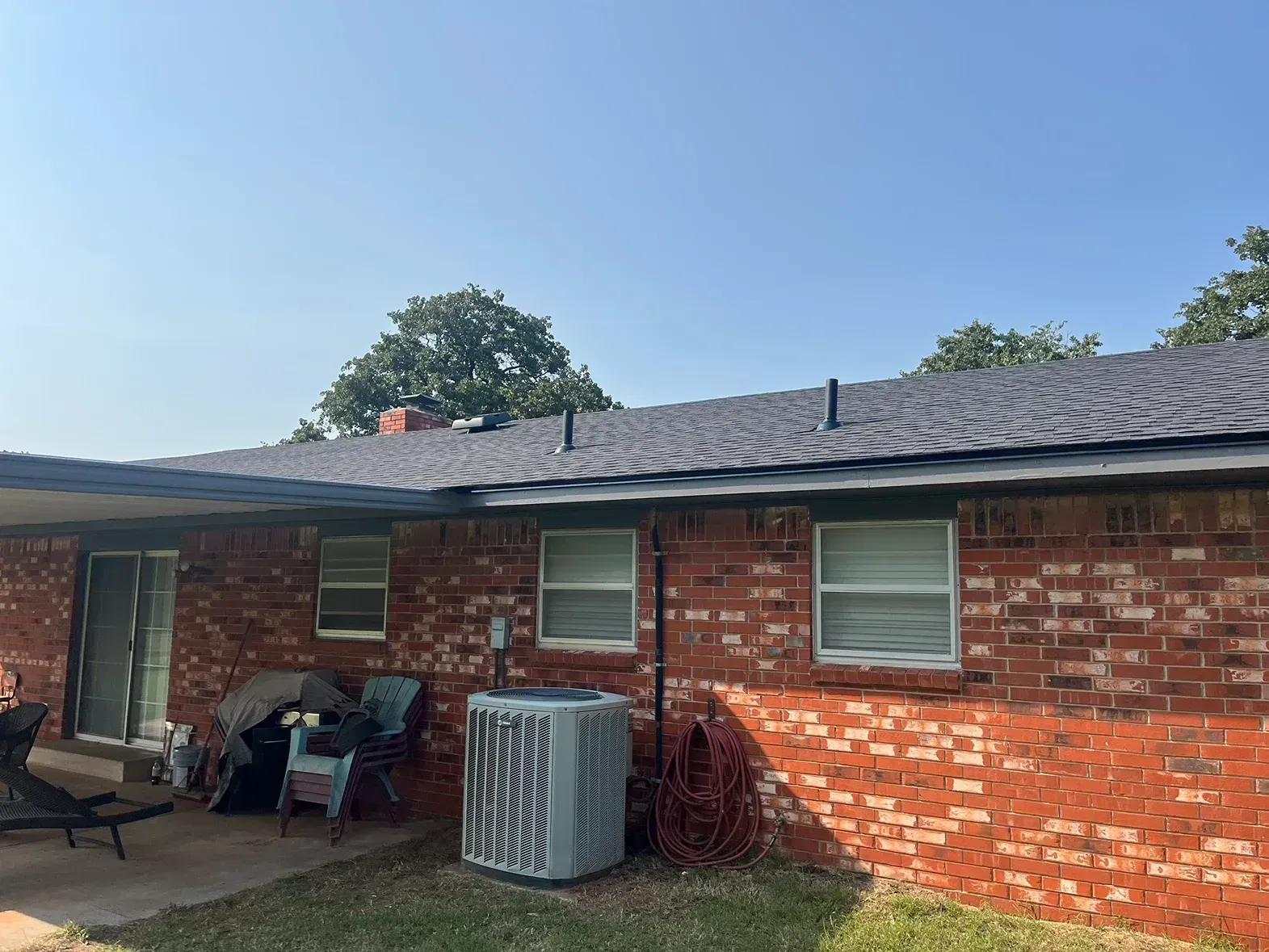Red brick house with dark roof, windows, and an AC unit.