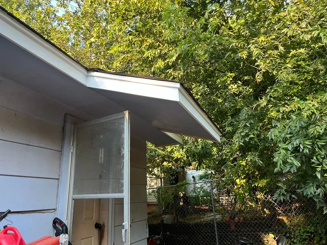 White building with an open window and a roof overhang. Trees are in the background.