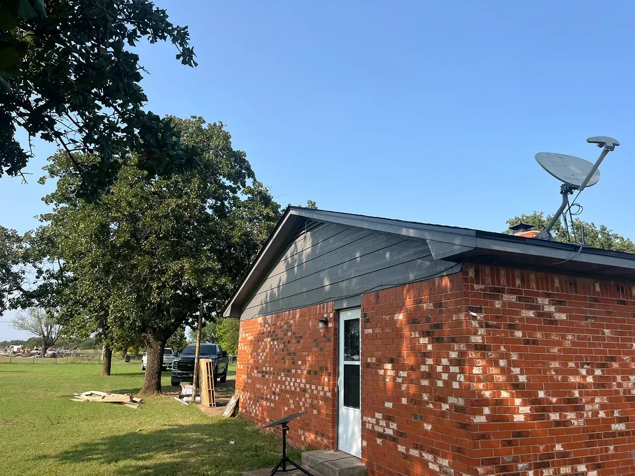 Brick building with dark roof, satellite dish, and tree under blue sky.