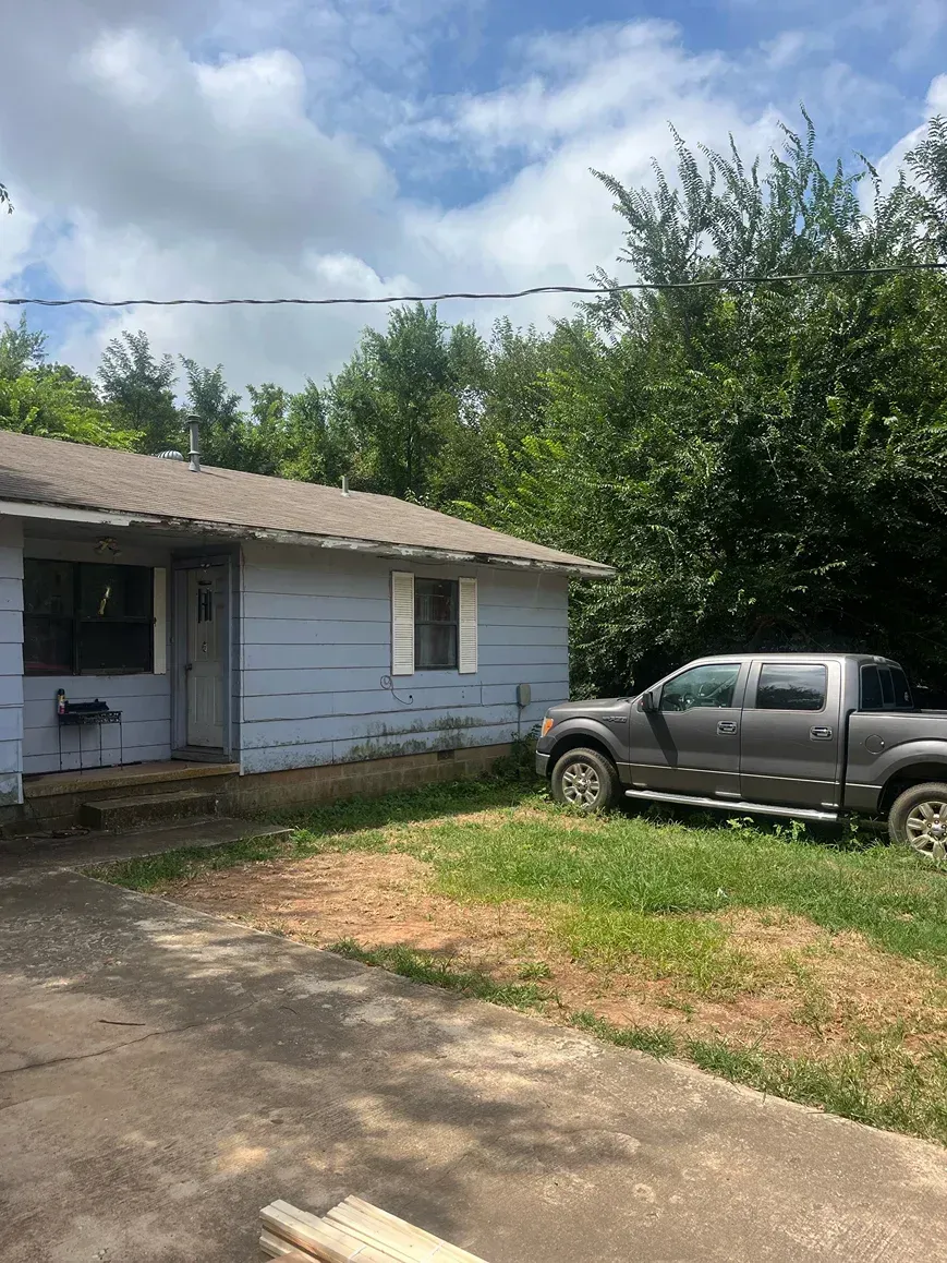 Blue house with truck parked on a driveway and grass area. Trees and cloudy sky in background.